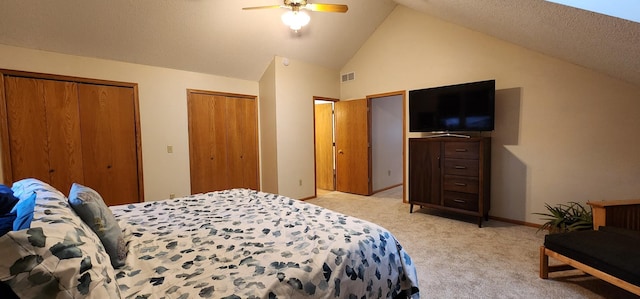 bedroom with lofted ceiling, visible vents, a ceiling fan, light carpet, and two closets