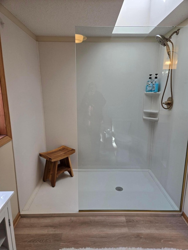 bathroom featuring a skylight, wood finished floors, and a walk in shower