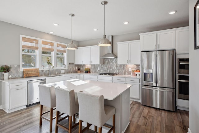 kitchen featuring wall chimney range hood, stainless steel appliances, a sink, and wood finished floors