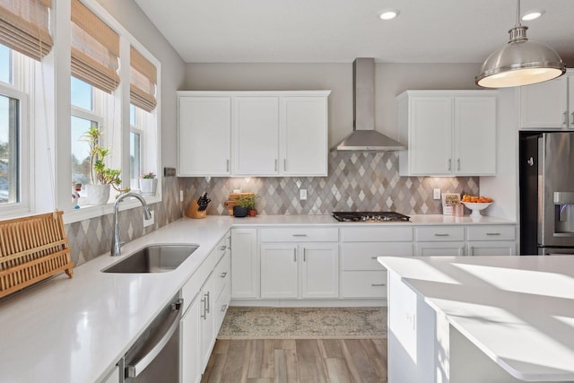 kitchen with tasteful backsplash, appliances with stainless steel finishes, white cabinetry, a sink, and wall chimney exhaust hood