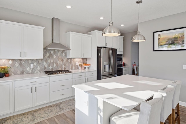 kitchen with light wood-style flooring, decorative backsplash, appliances with stainless steel finishes, white cabinetry, and wall chimney range hood