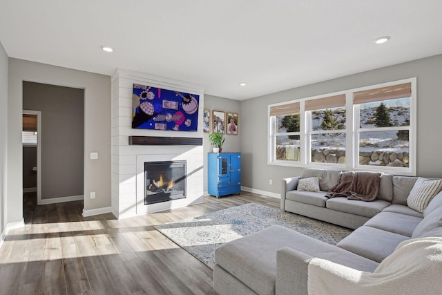 living area featuring recessed lighting, a large fireplace, baseboards, and wood finished floors