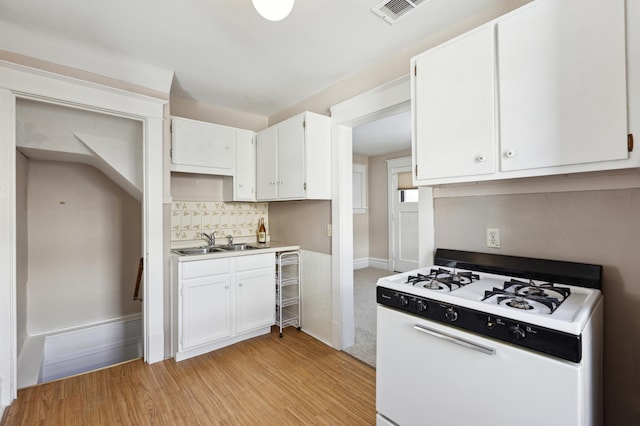 kitchen featuring light wood finished floors, decorative backsplash, white cabinetry, a sink, and white gas range oven