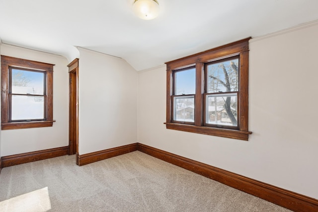 carpeted spare room with lofted ceiling, baseboards, and crown molding