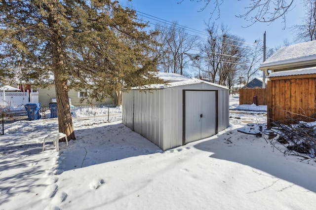 snow covered structure featuring an outdoor structure, fence, and a storage unit