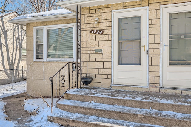 snow covered property entrance featuring stone siding