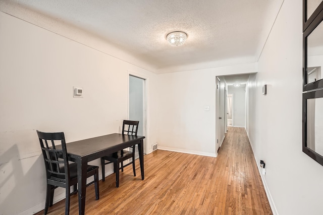 dining room with a textured ceiling, baseboards, and light wood-style floors