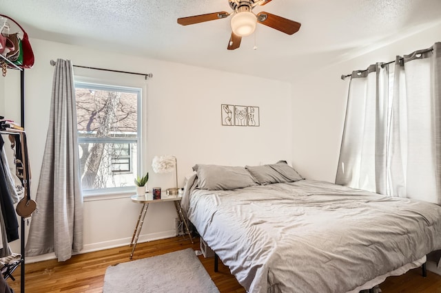 bedroom with ceiling fan, a textured ceiling, baseboards, and wood finished floors