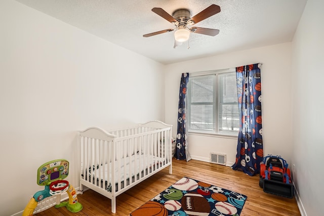 bedroom with baseboards, visible vents, wood finished floors, a textured ceiling, and a nursery area