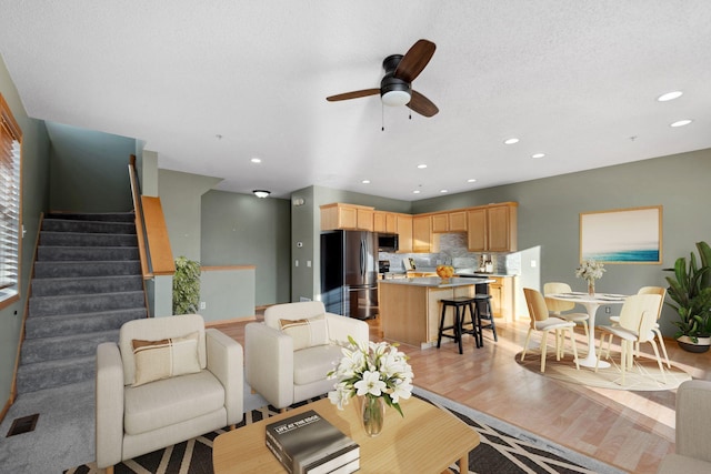 living room with visible vents, light wood-style flooring, recessed lighting, ceiling fan, and stairs