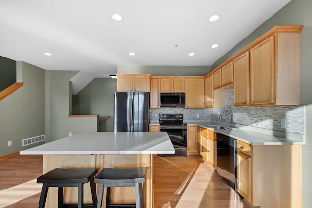 kitchen with visible vents, a center island, light brown cabinetry, stainless steel appliances, and a sink