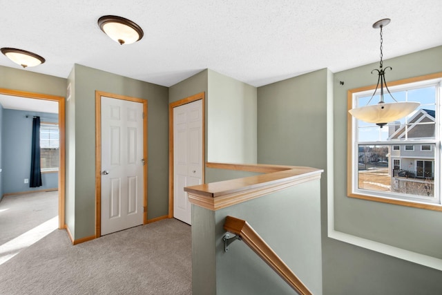 corridor with an upstairs landing, a healthy amount of sunlight, a textured ceiling, and carpet floors