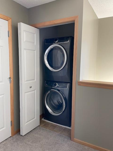 clothes washing area with baseboards, carpet floors, laundry area, stacked washer and clothes dryer, and a textured ceiling