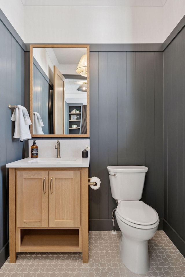 half bathroom featuring toilet, vanity, and a decorative wall