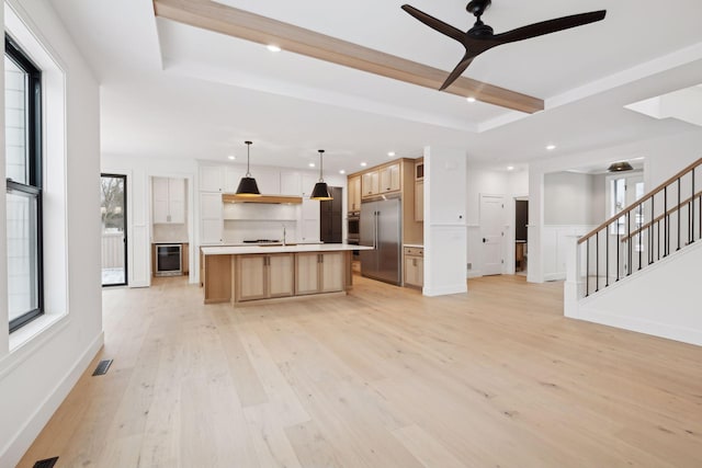 unfurnished living room with light wood-type flooring, ceiling fan, recessed lighting, wine cooler, and a tray ceiling