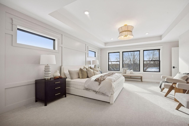 bedroom featuring light colored carpet, multiple windows, and a tray ceiling