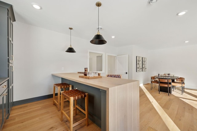 bar featuring light wood-type flooring, baseboards, recessed lighting, and decorative light fixtures