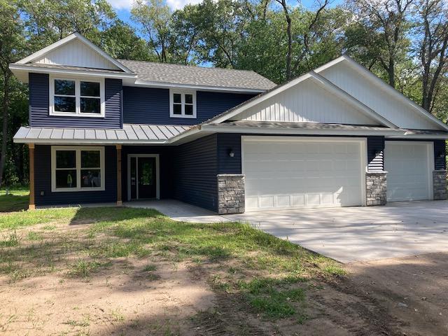 view of front facade with driveway, stone siding, roof with shingles, an attached garage, and a standing seam roof