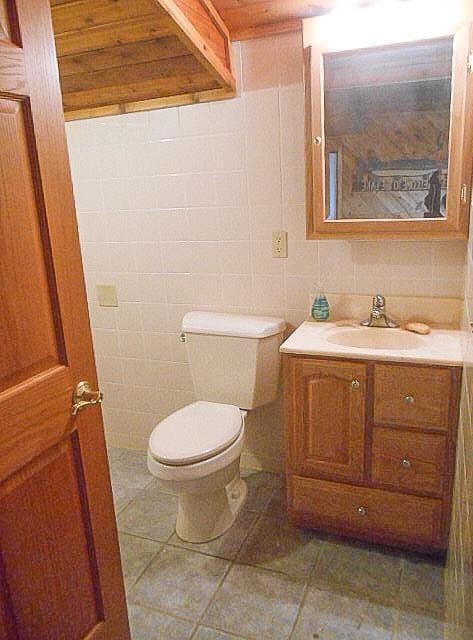 half bathroom with tile patterned flooring, tile walls, toilet, and vanity