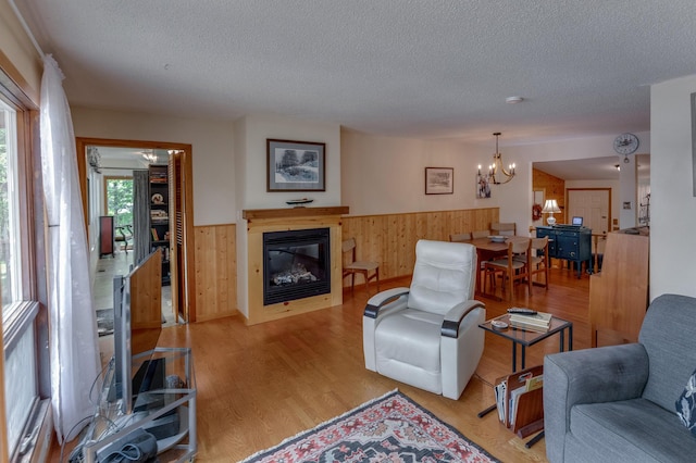 living room with a chandelier, wainscoting, wood finished floors, a glass covered fireplace, and a textured ceiling