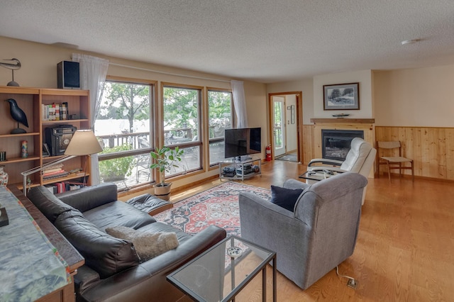 living room with wooden walls, wainscoting, wood finished floors, a glass covered fireplace, and a textured ceiling