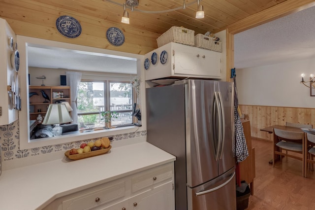 kitchen with a wainscoted wall, white cabinetry, freestanding refrigerator, an inviting chandelier, and wood walls