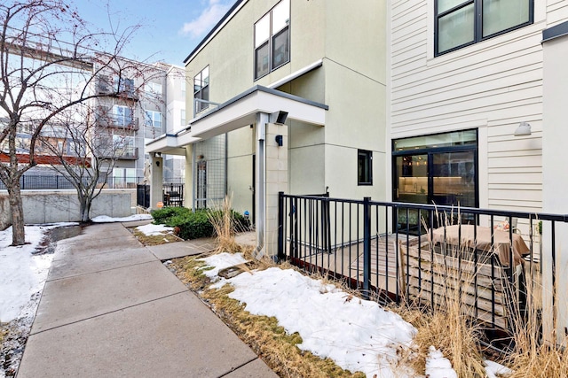 snow covered property entrance featuring stucco siding and fence