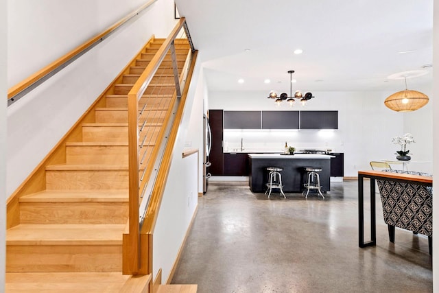 stairway with recessed lighting, baseboards, concrete flooring, and a chandelier