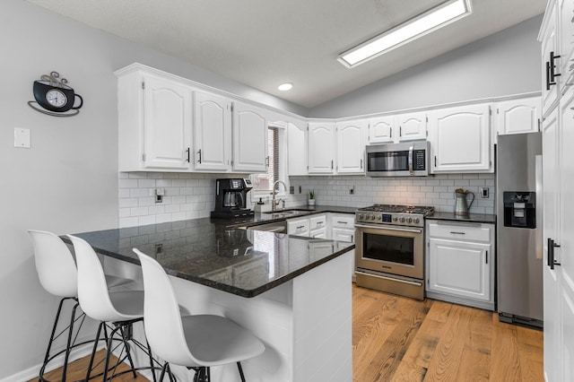 kitchen with stainless steel appliances, white cabinets, vaulted ceiling, a sink, and a peninsula