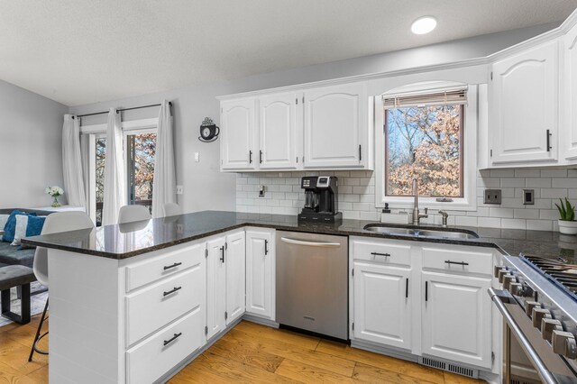 kitchen featuring stainless steel appliances, a peninsula, a sink, white cabinets, and light wood-type flooring