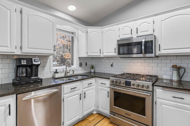 kitchen with lofted ceiling, a sink, white cabinets, appliances with stainless steel finishes, and dark stone countertops