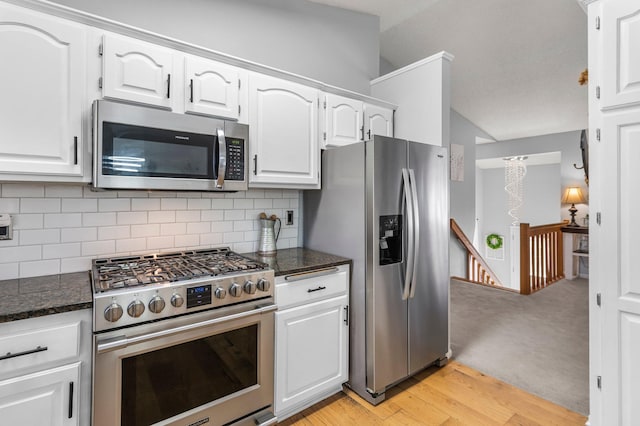 kitchen featuring light wood finished floors, white cabinets, dark stone countertops, stainless steel appliances, and backsplash