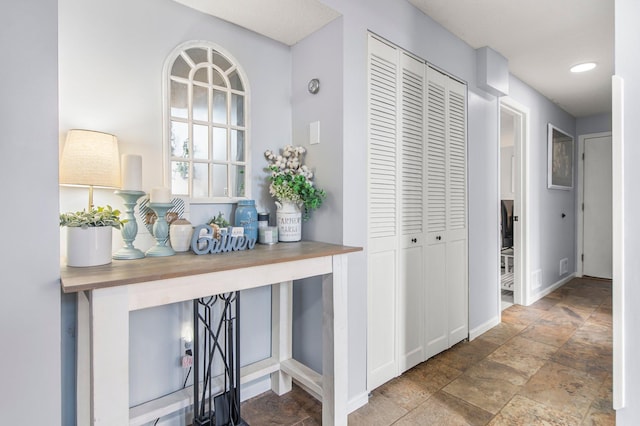 corridor featuring stone finish flooring and baseboards