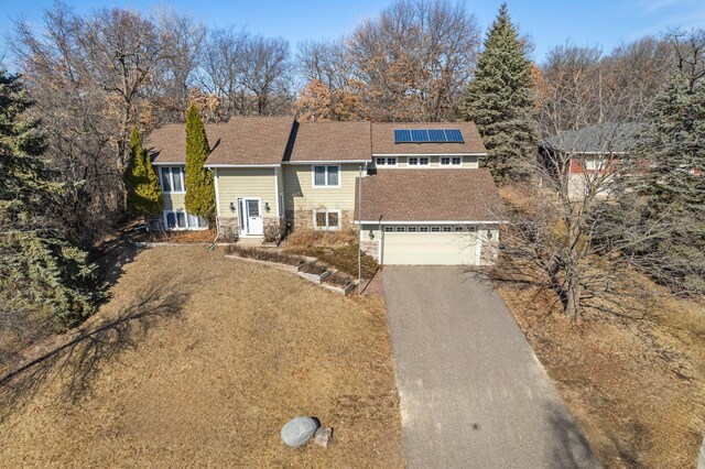 view of front of house featuring a garage, roof mounted solar panels, driveway, and stone siding