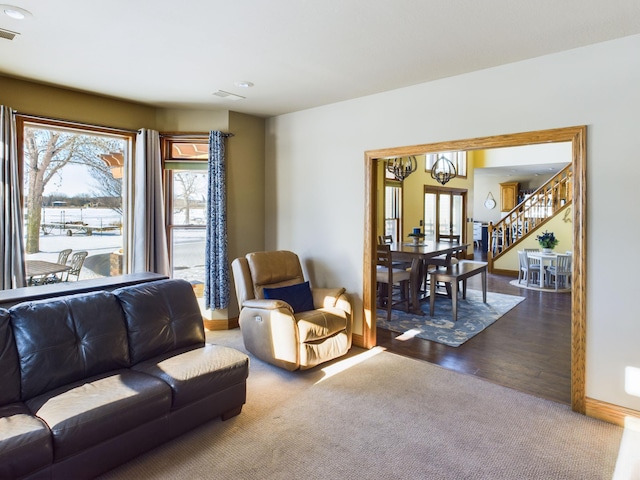 living area with a notable chandelier, dark colored carpet, visible vents, stairway, and baseboards