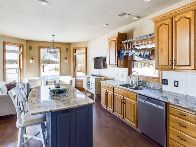 kitchen with pendant lighting, dark wood finished floors, stainless steel dishwasher, a kitchen island, and a sink