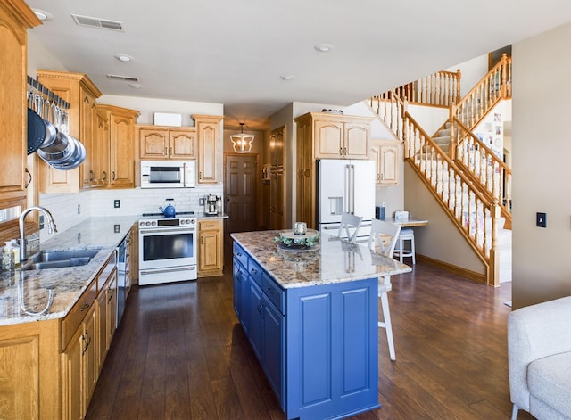 kitchen with white appliances, a breakfast bar, a kitchen island, visible vents, and a sink