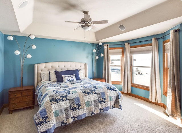 carpeted bedroom with a tray ceiling, a ceiling fan, and baseboards