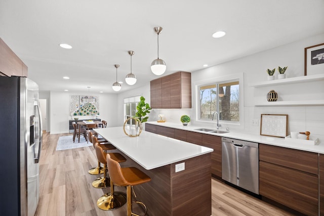 kitchen with a sink, light countertops, appliances with stainless steel finishes, a kitchen breakfast bar, and modern cabinets