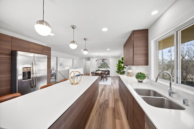 kitchen with light countertops, stainless steel refrigerator with ice dispenser, hanging light fixtures, modern cabinets, and a sink