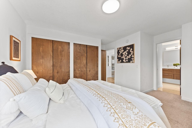 bedroom with baseboards, multiple closets, light carpet, ensuite bathroom, and a sink