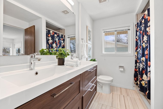 bathroom featuring a healthy amount of sunlight, visible vents, double vanity, a sink, and toilet