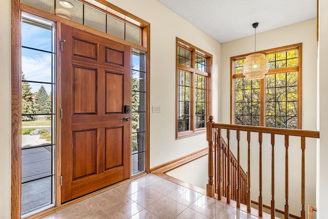 foyer with light tile patterned flooring, a textured ceiling, and baseboards