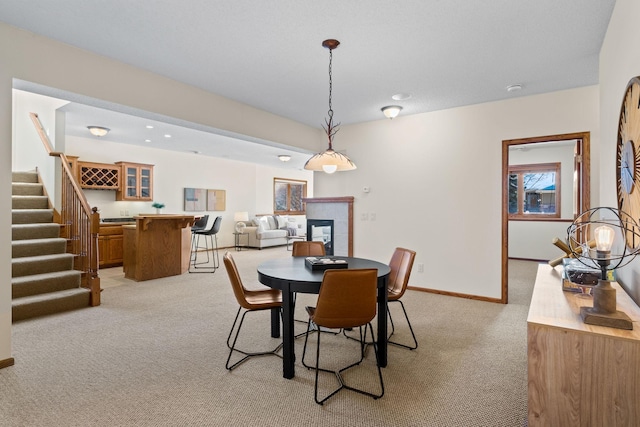 dining space featuring stairs, baseboards, a tiled fireplace, and light colored carpet