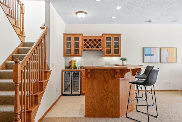 bar with a textured ceiling, wine cooler, indoor wet bar, and baseboards