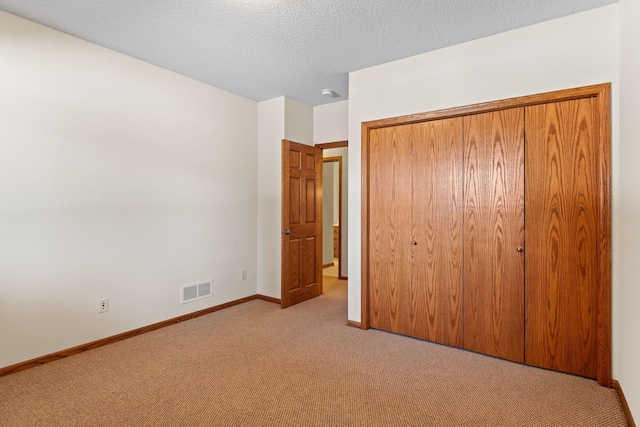 unfurnished bedroom with a closet, light colored carpet, visible vents, a textured ceiling, and baseboards