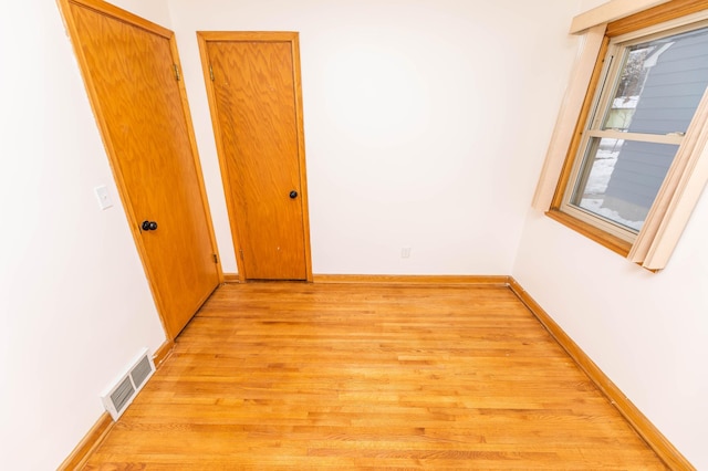 empty room with light wood finished floors, visible vents, and baseboards