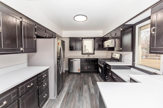 kitchen featuring a sink, dark brown cabinets, light countertops, stainless steel appliances, and dark wood-style flooring