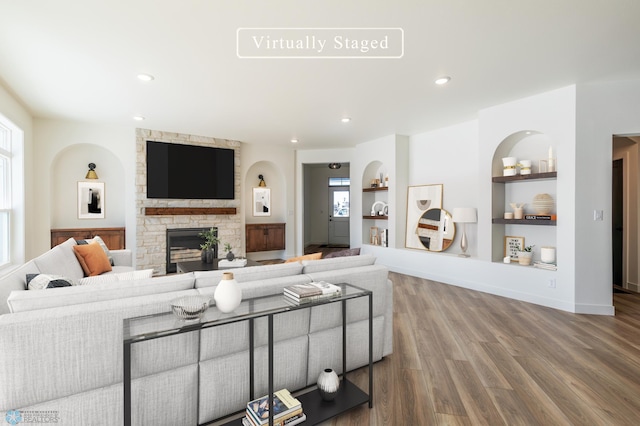 living area with built in shelves, baseboards, a stone fireplace, recessed lighting, and wood finished floors