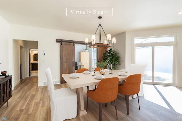 dining room featuring a barn door, light wood-style flooring, a notable chandelier, and baseboards